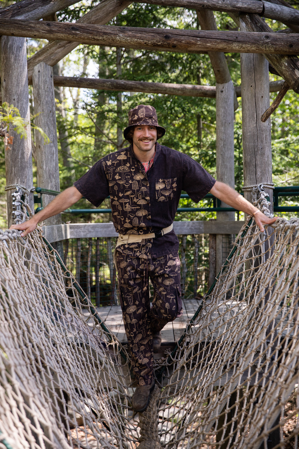 A handsome man with a mustache crossing a rope bridge in a brown matching mushroom outfit