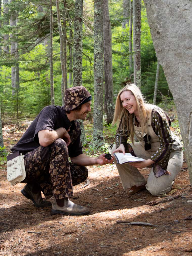 A man and a woman on a psychedelic exploration in the forest wearing matching earth tone mushroom patterned clothing with a spiral carved stone tower in the foreground