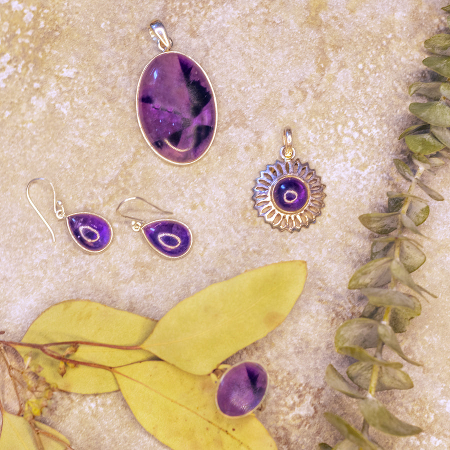 a selection of glimmering amethyst jewelry set in sterling silver on yellow leaf petals and a granite backdrop