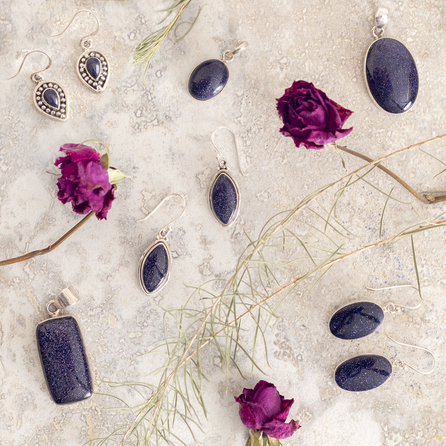 a collection of shimmering blue goldstone jewelry surrounded by flower petals on a granite backdrop