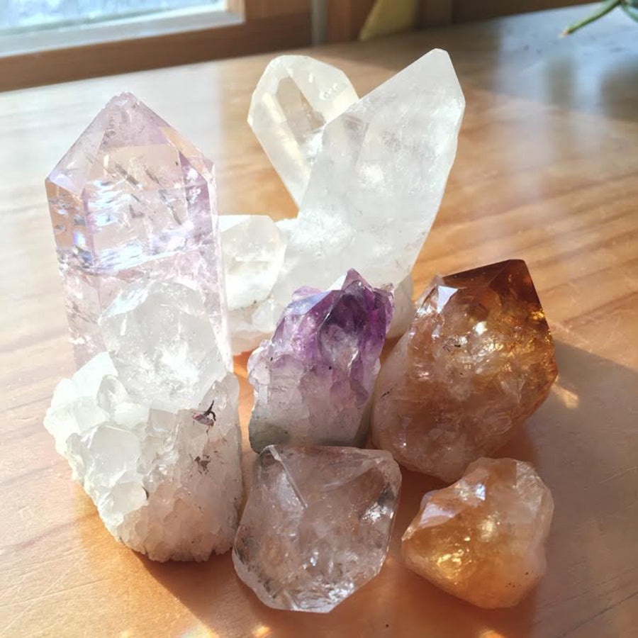 a collection of rough cut crystals being cleansed by sunshine in a window on a wooden background