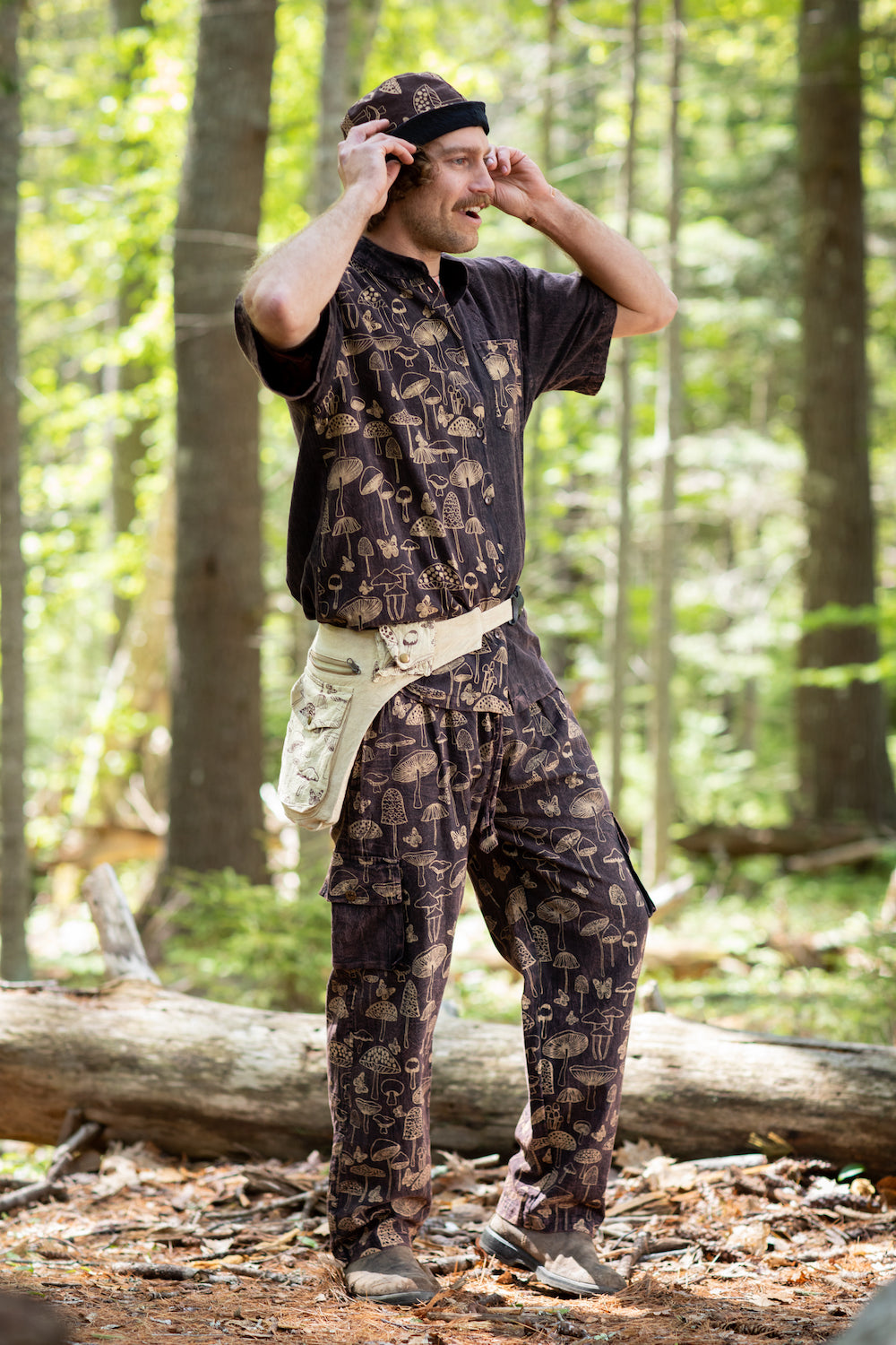An adventurous man in the forest wearing a matching mushroom outfit with a mushroom print button up shirt, mushroom bucket hat, mushroom satchel, and mushroom pants 