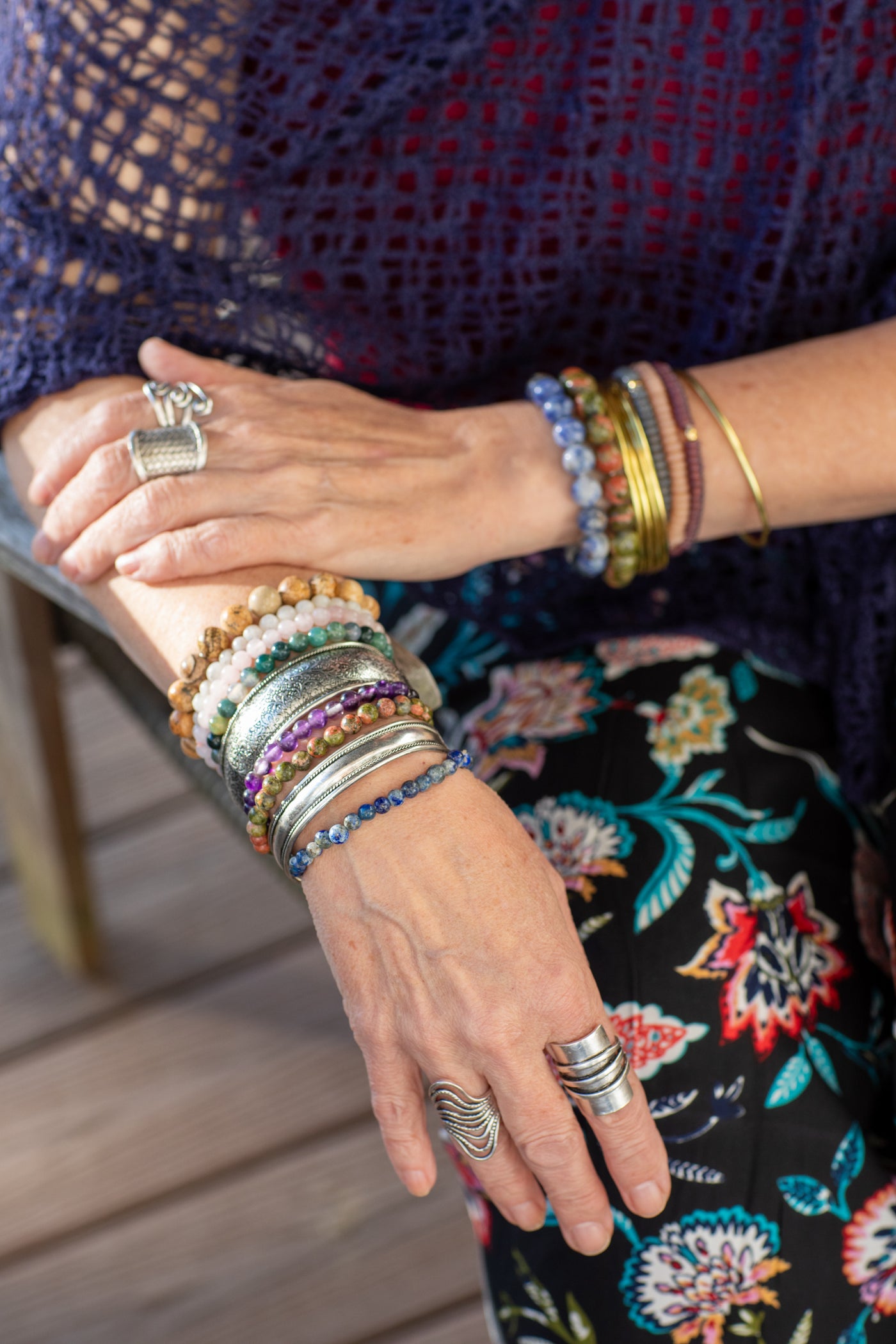 Close-up of hand swearing multiple bracelets and rings with a floral-patterned pants.