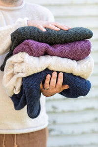 Person holding a stack of folded alpaca sweaters in various colors.