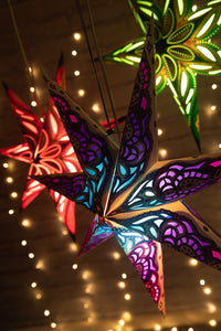 A set of three 7-pointed star lanterns in red, purple, and green, lit up and glowing with a twinkling backdrop. 