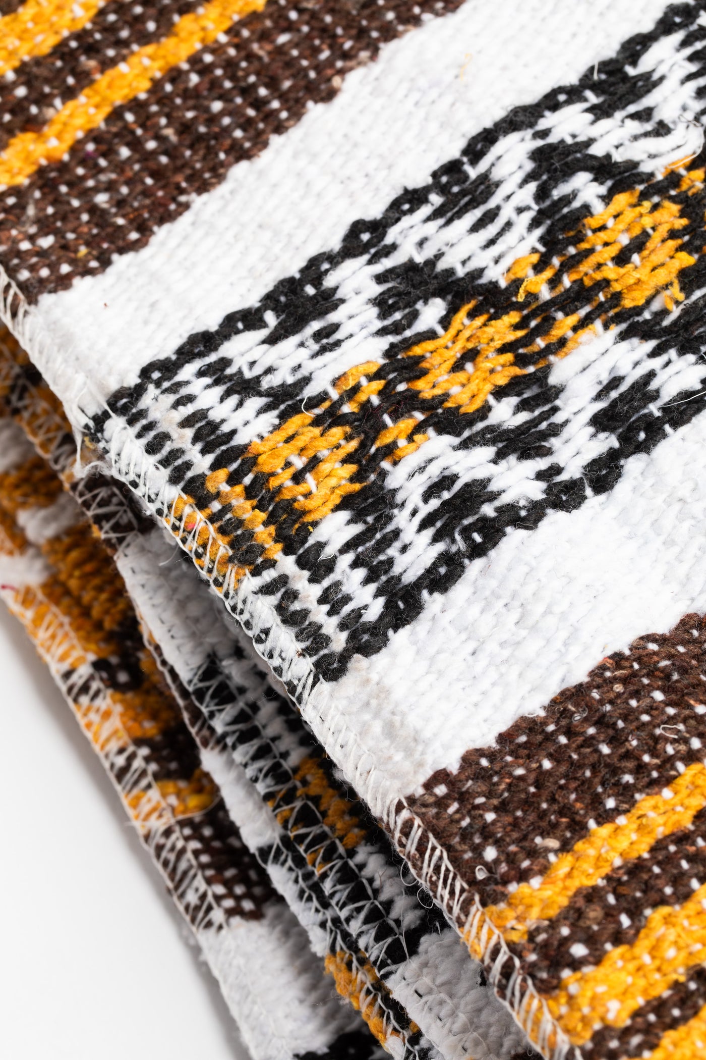 Woven recycled yarn blanket with yellow, brown, and white patterns on a white background
