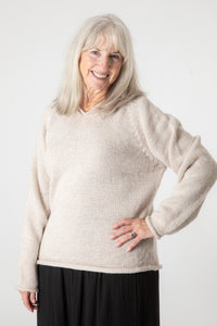 Toni, wearing size S, smiling and wearing an oatmeal alpaca wool pullover sweater with a hood.