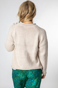 Sophie wearing a size medium oatmeal fisherman style sweater with a plain background