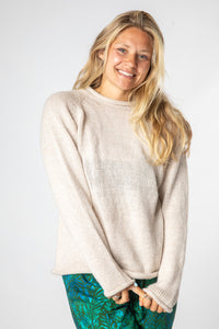 Sophie wearing a size medium oatmeal fisherman style sweater with a plain background