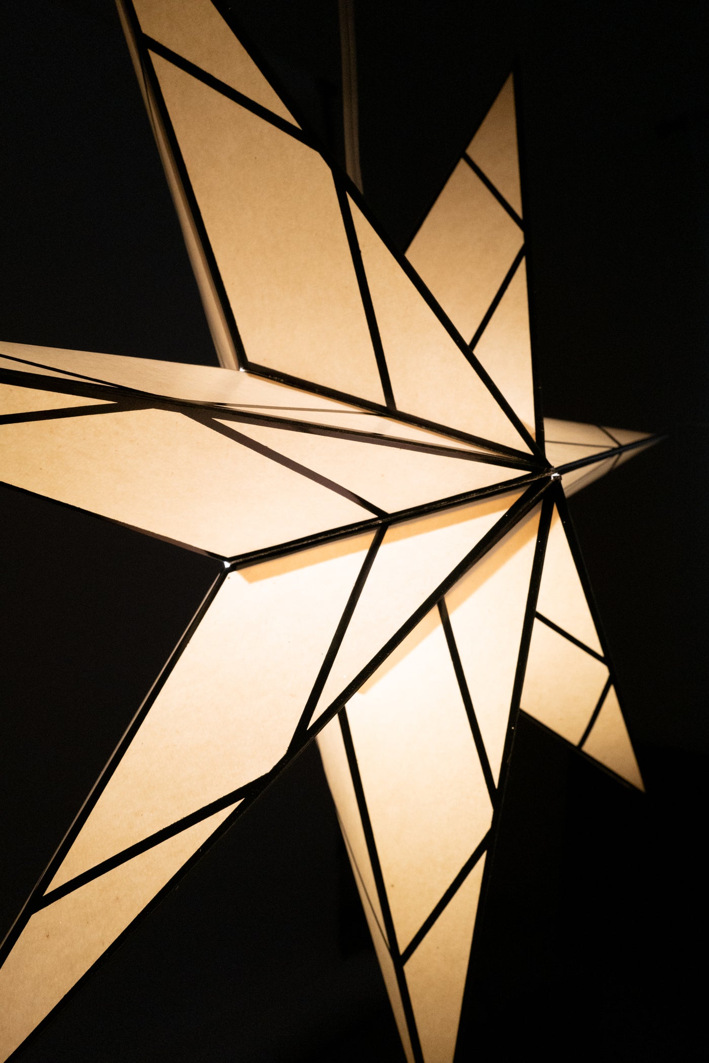 A detailed shot of a white and black paper star lantern with a glass effect illuminated and glowing in a dark room. 