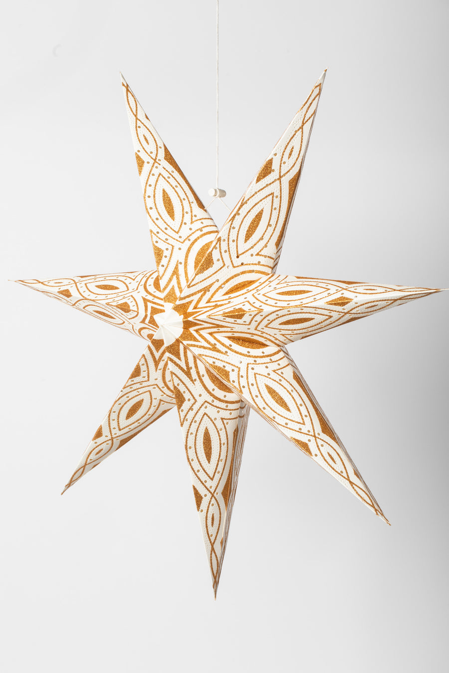 A hanging 7-point paper star lantern in a white and gold intricate pattern hanging in front of a white background. Light kit sold separately.