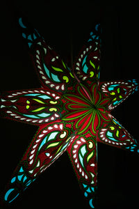 A close up shot of a glowing pink and green paper star lantern illuminated in a dark room. 