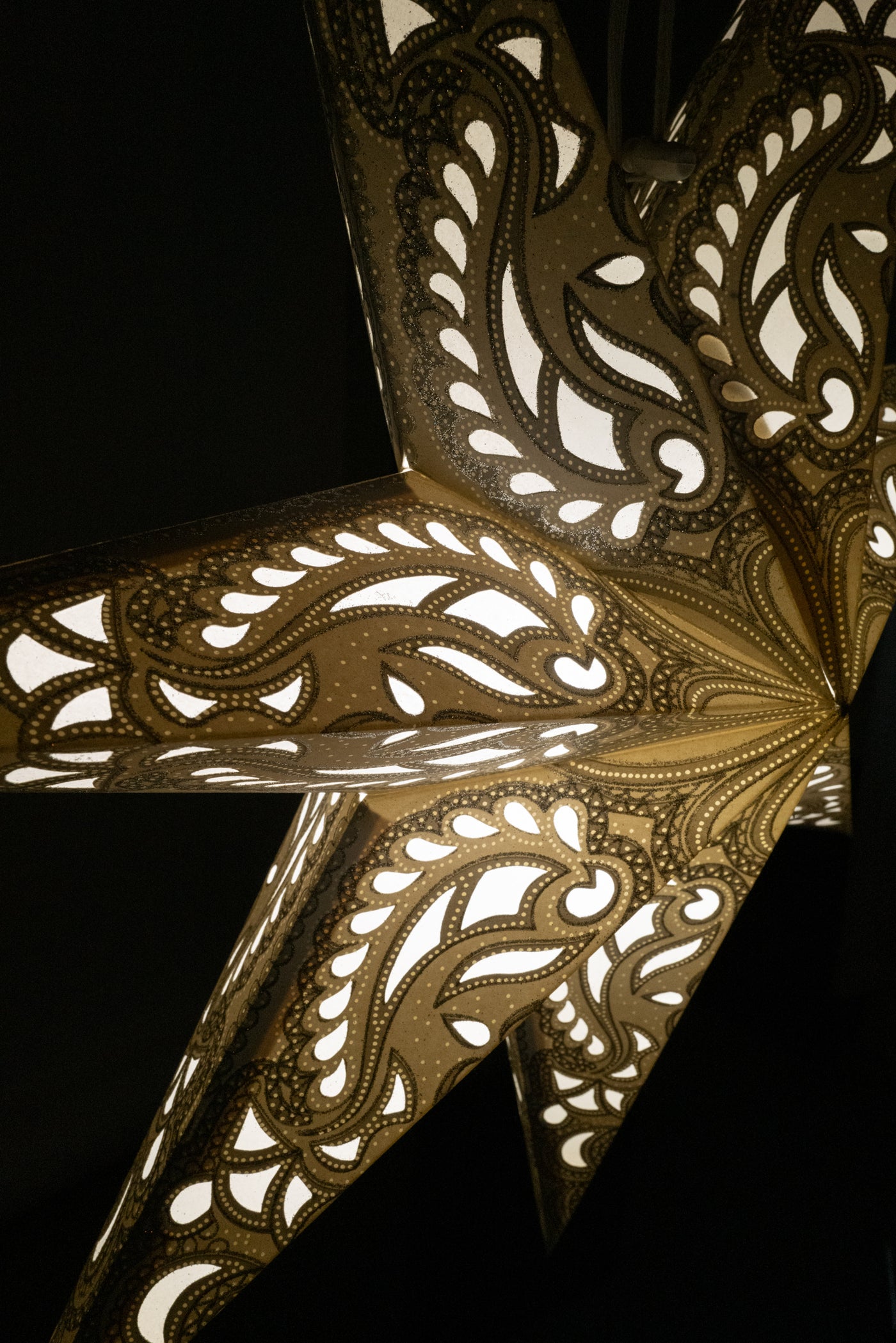 A close up image of a glowing white paper star lantern with an intricate design illuminated in a dark room. 