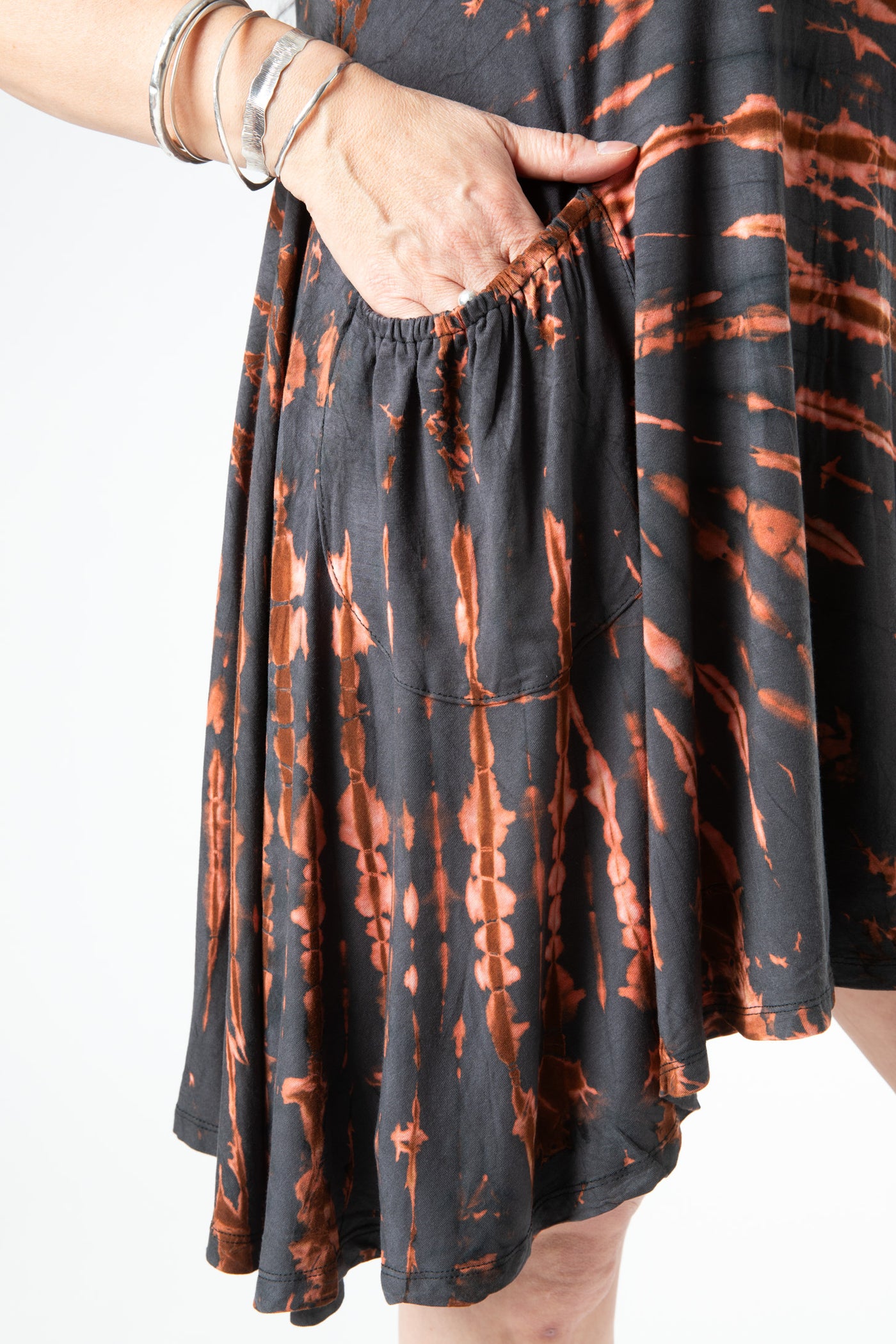 Detailed image of the pocket on this tie dye dress in a gray tie dye pattern on a woman with her hand in the pocket wearing silver bracelets 