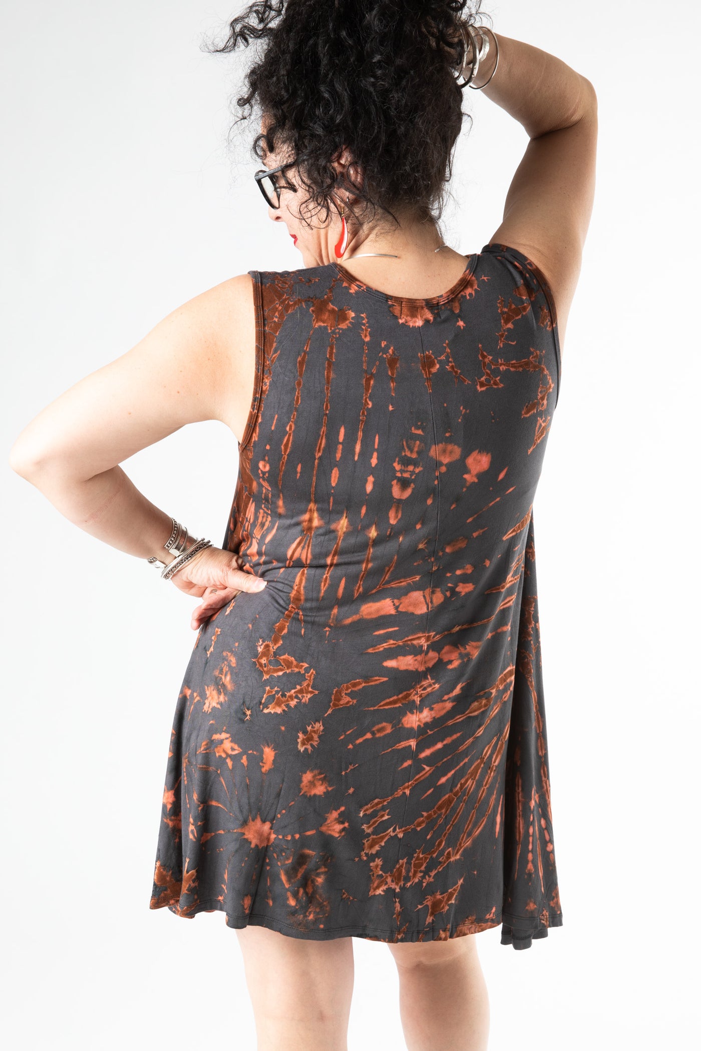 Curly haired woman facing backwards wearing a sleeveless tie dye dress in a gray tie dye pattern 