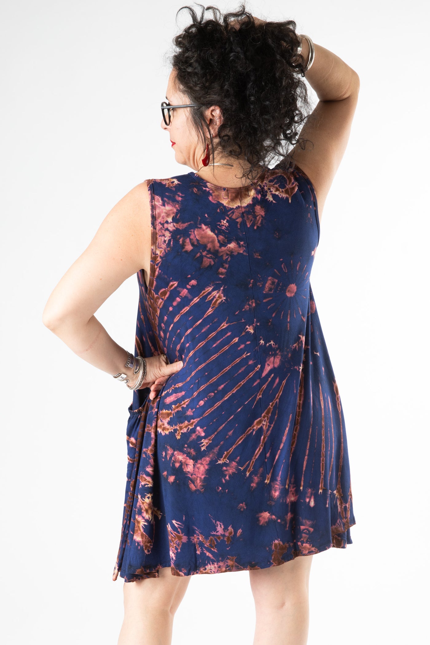 Dark curly haired woman facing backwards wearing a blue sleeveless tie dye dress 