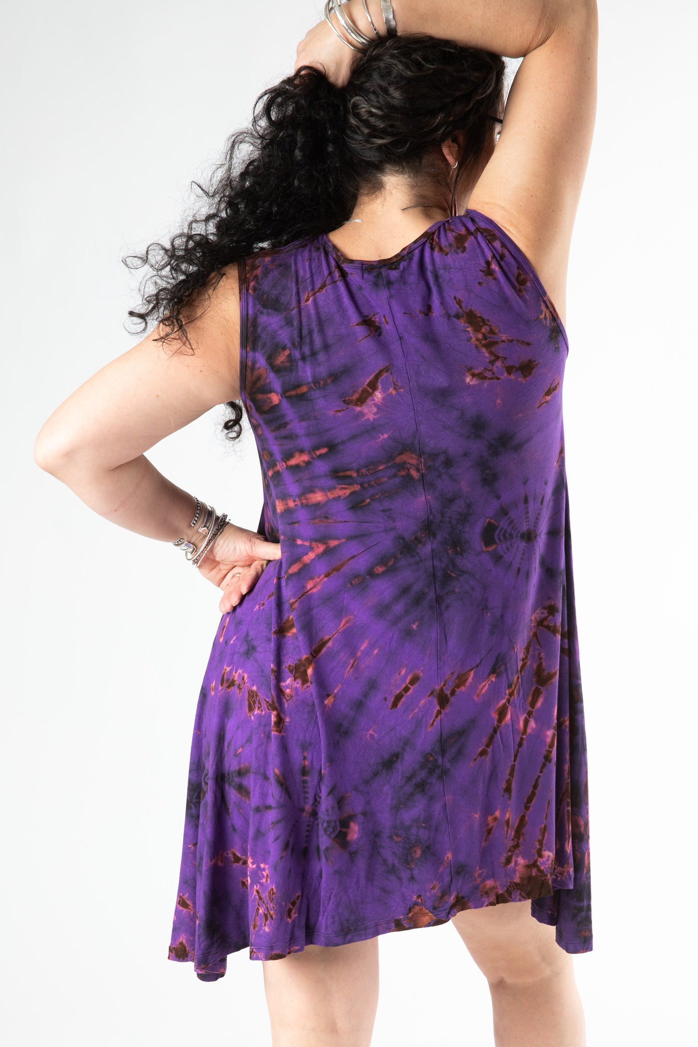 Dark haired woman facing backwards wearing a sleeveless tie dye dress in a purple tie dye pattern 