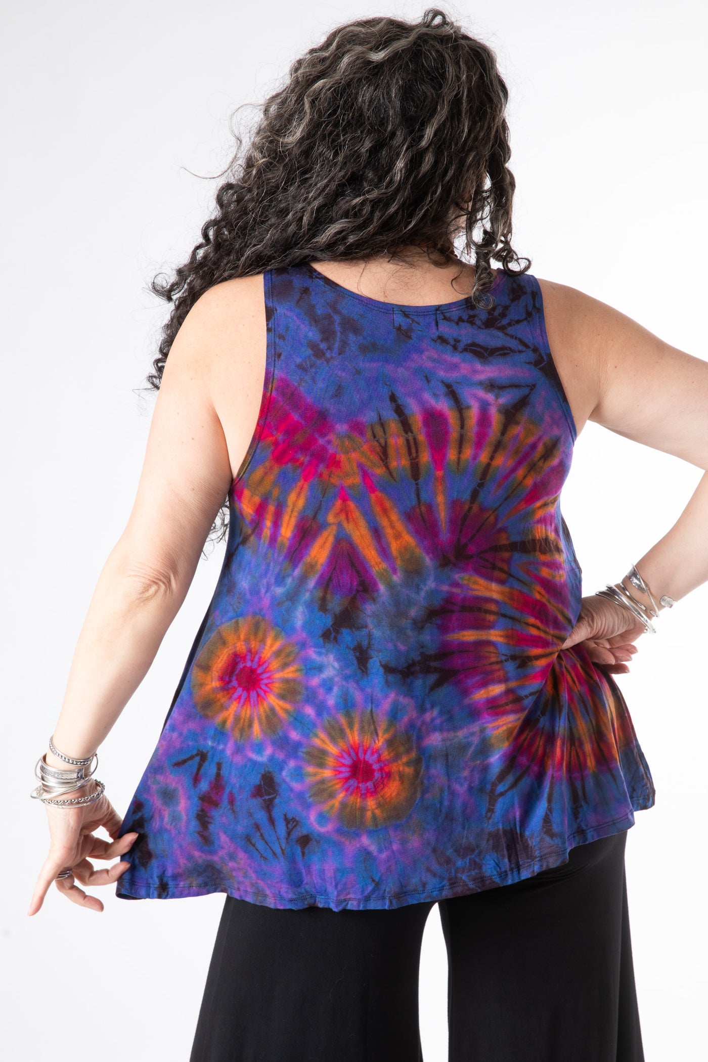 Curly haired woman facing backwards wearing a purple tie dye tank top and black wide leg pants 