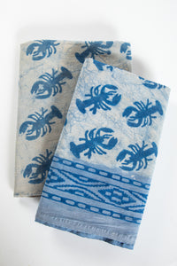 A beige decorative tapestry with a blue lobster pattern, folded and displayed on a flat surface.