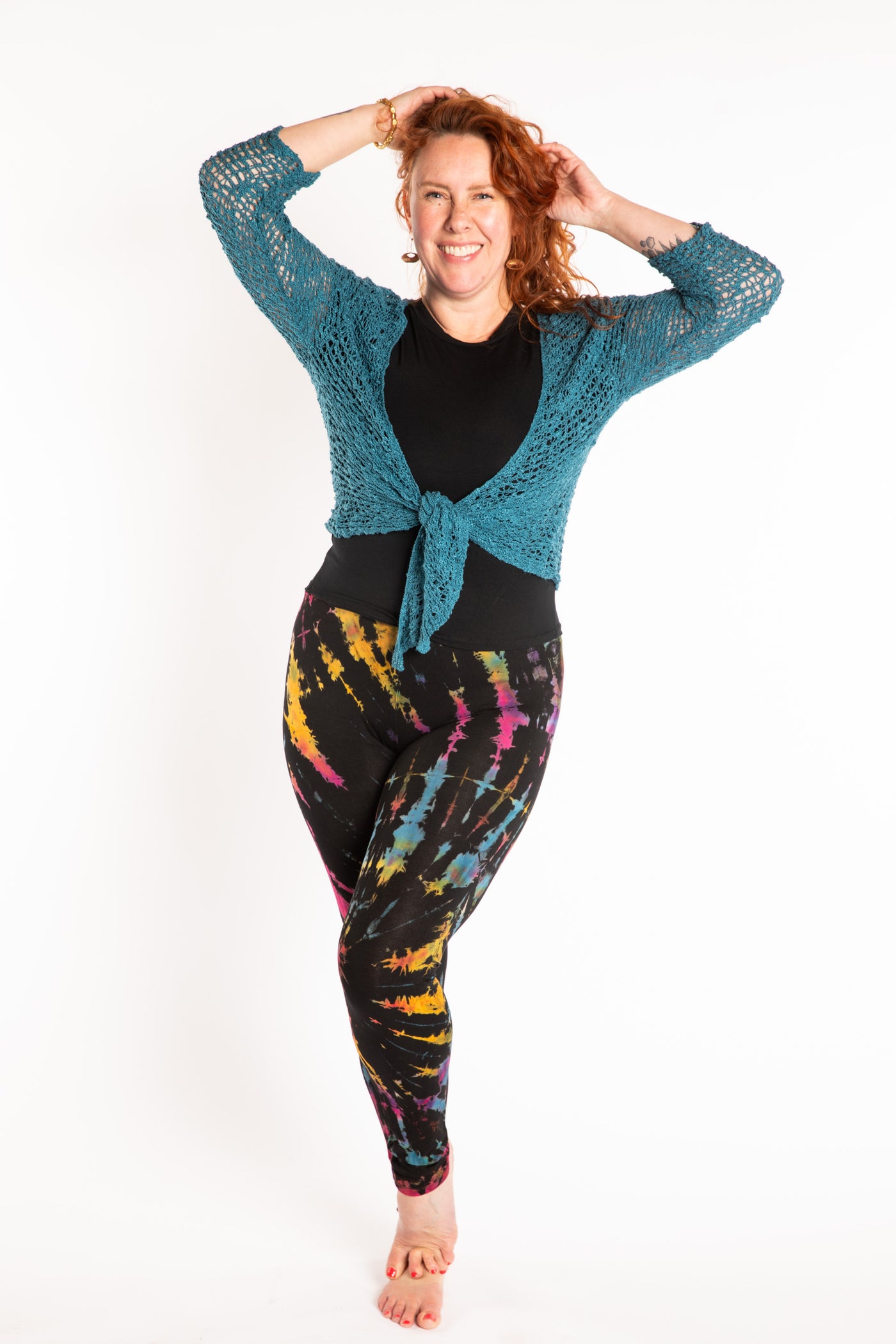 Maggie is wearing the size M/L Black Rainbow Tie Dye Leggings, size L Chara Crew Neck Top in Black and Talia Loose Weave Wrap Cardigan in Teal