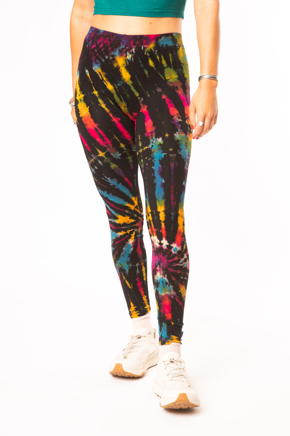 Hippie girl wearing black rainbow tie dye leggings with a teal crop top and white sneakers 