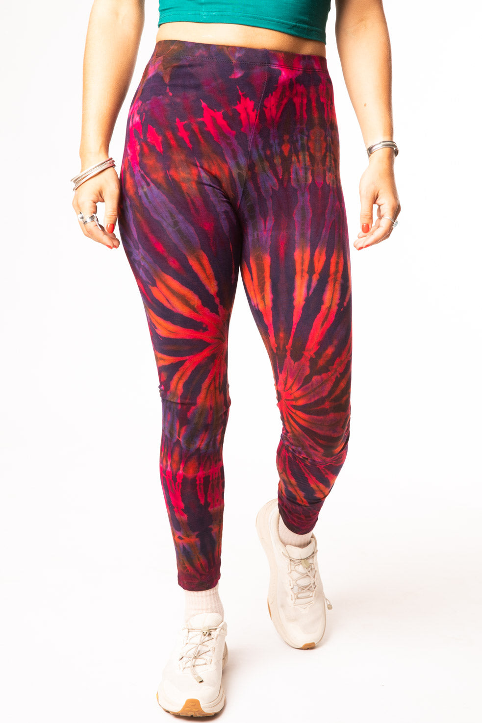 A female model wearing colorful tie dye leggings in purple, pink, and orange, with a teal crop top and white sneakers