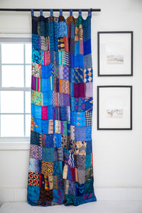 Colorful patchwork curtain in Blue hanging in front of a window with framed pictures on the wall.