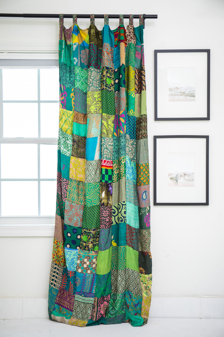 Colorful patchwork curtain in Green hanging in a room with white walls and a window.