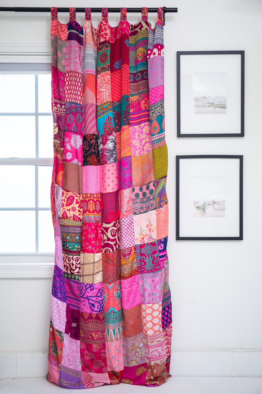 Colorful Pink patchwork curtain hanging in a room with framed pictures on the wall.