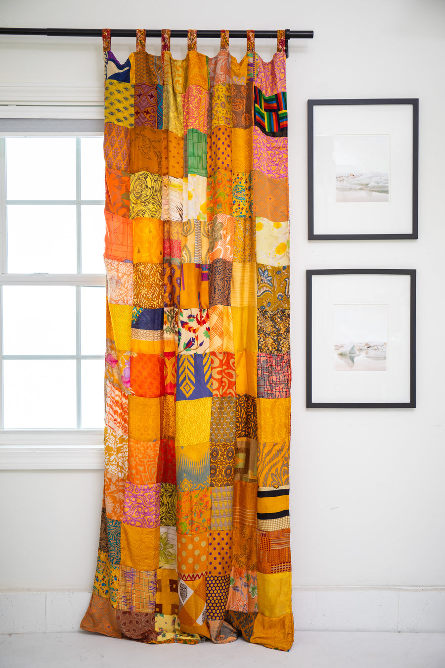 Colorful Yellow patchwork curtain hanging in front of a window with framed pictures on the wall.