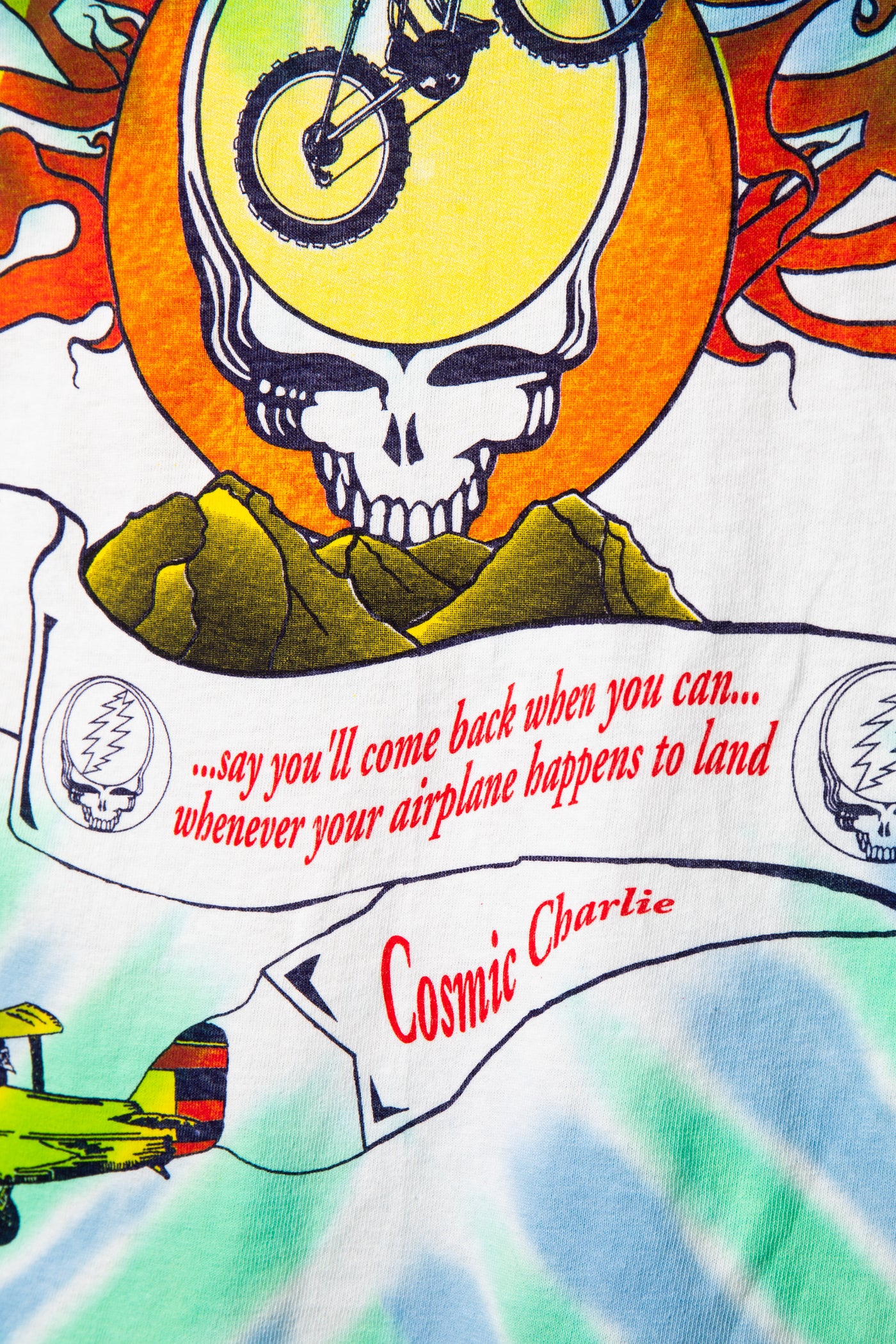 Colorful tie-dye shirt with a skull design, text, and airplane graphic.