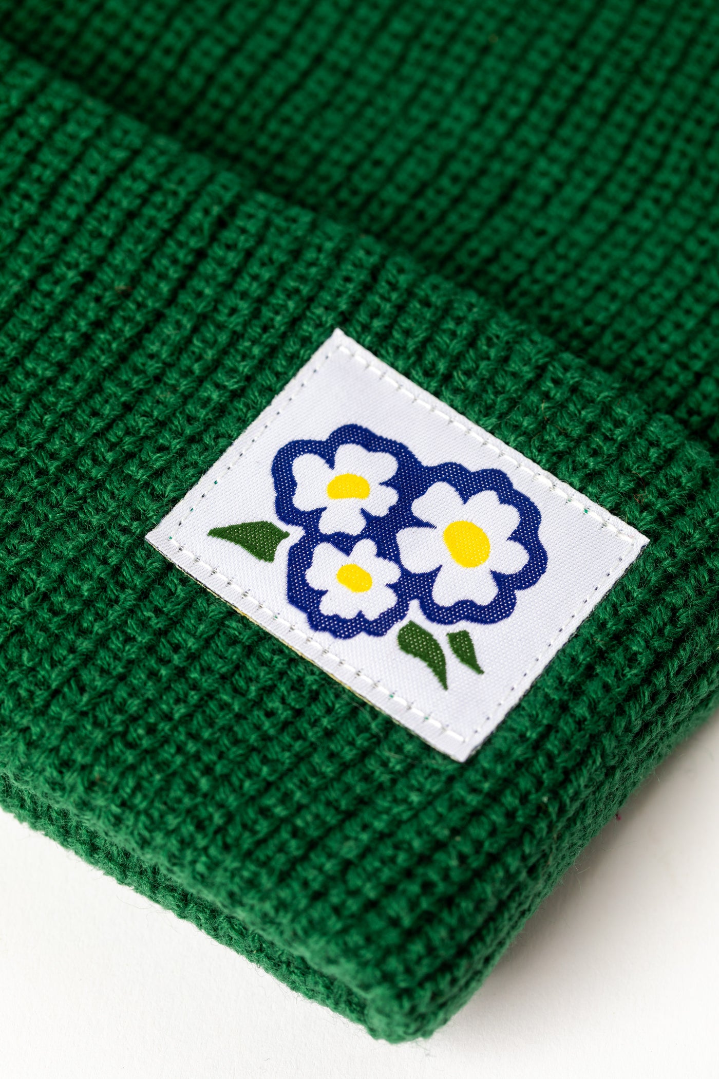 Detail of Forest Green knit acrylic beanie with a floral patch