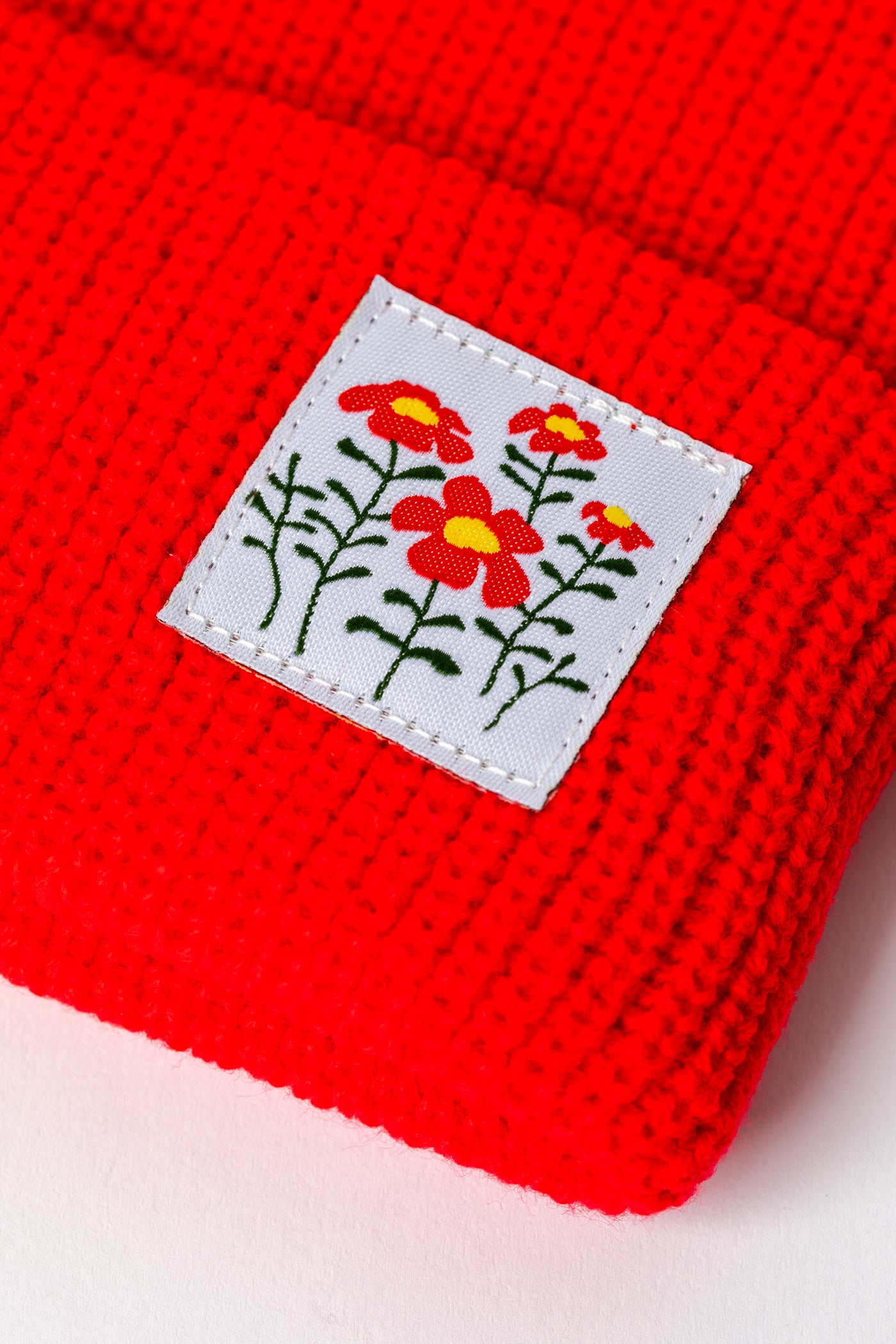 Detail of Orange Red knit acrylic beanie with a wildflower patch