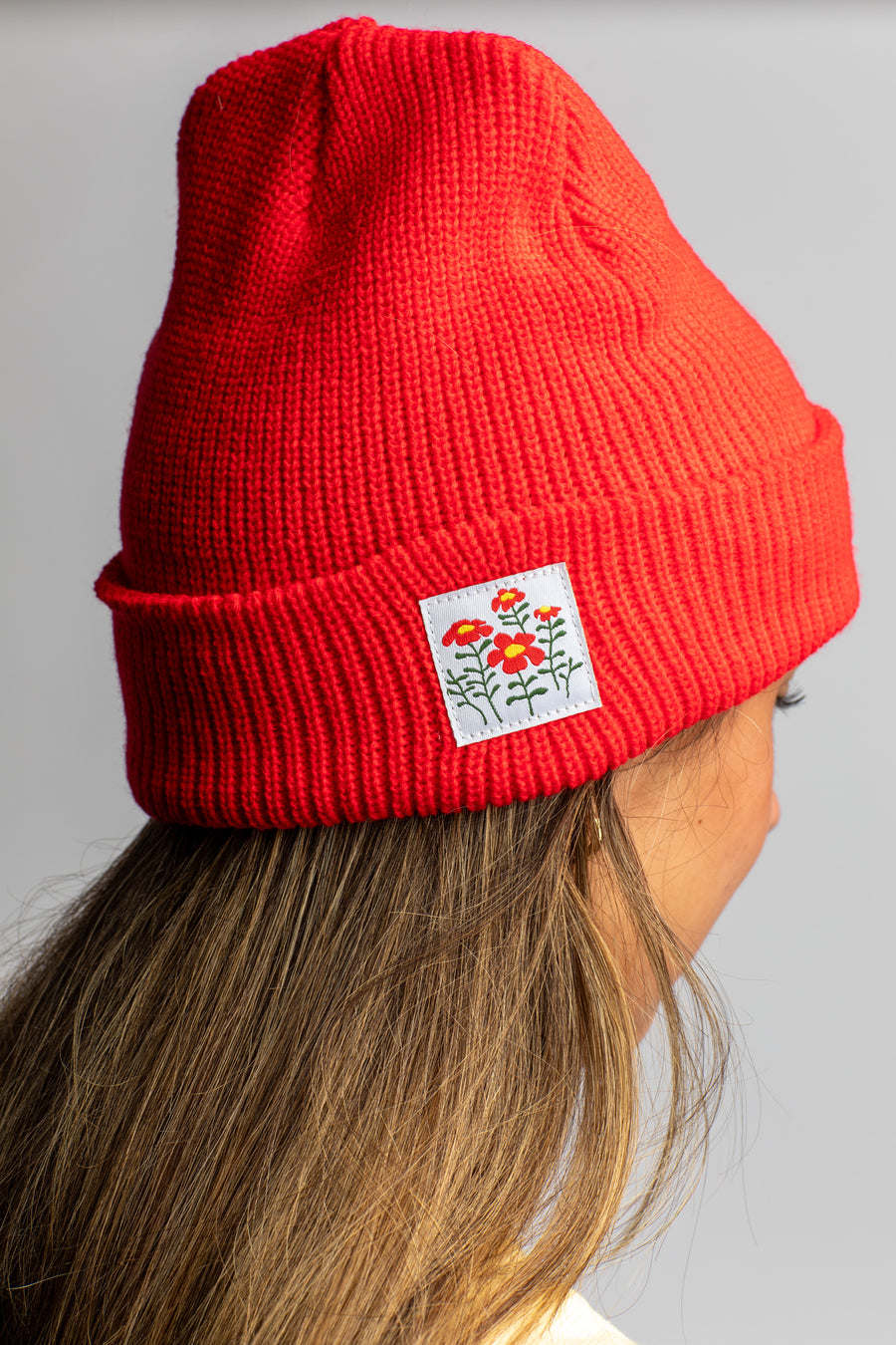 Lea wearing the Orange Red knit acrylic beanie with a wildflower patch