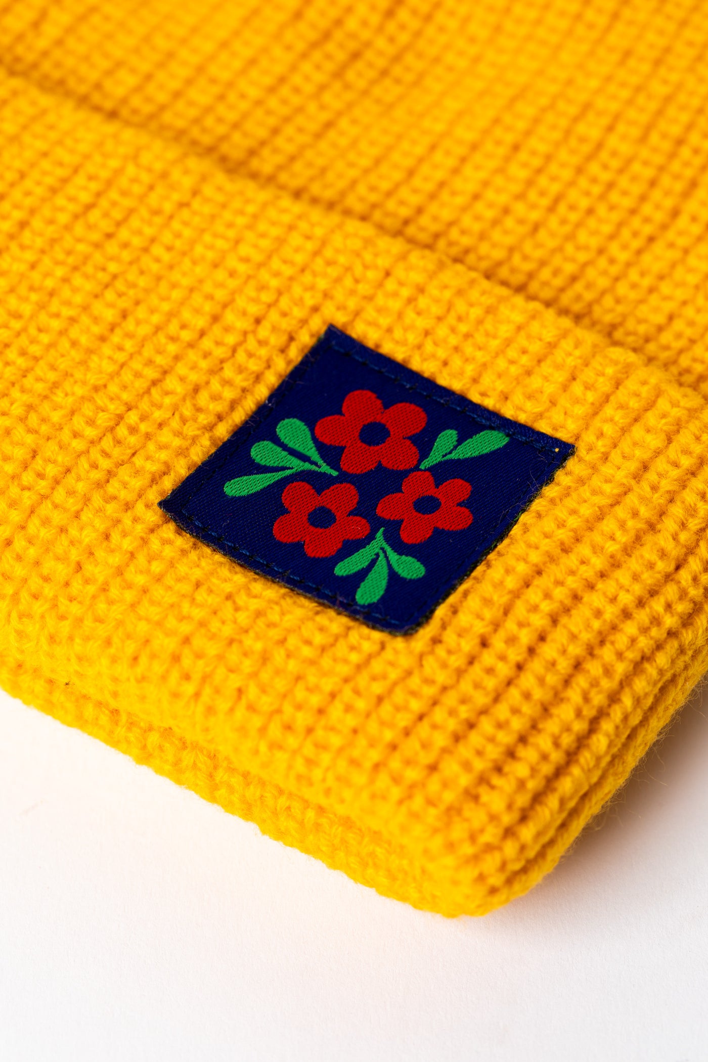 Detail of Yellow knit acrylic beanie with a floral patch