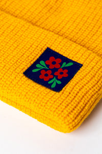 Detail of Yellow knit acrylic beanie with a floral patch