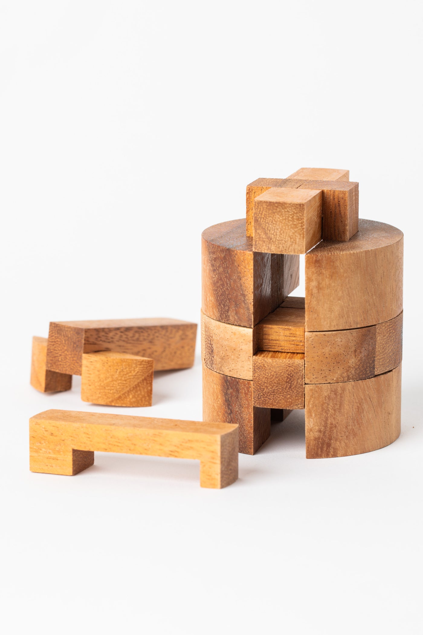 Partially assembled wooden cylinder puzzle with separate interlocking pieces beside it.