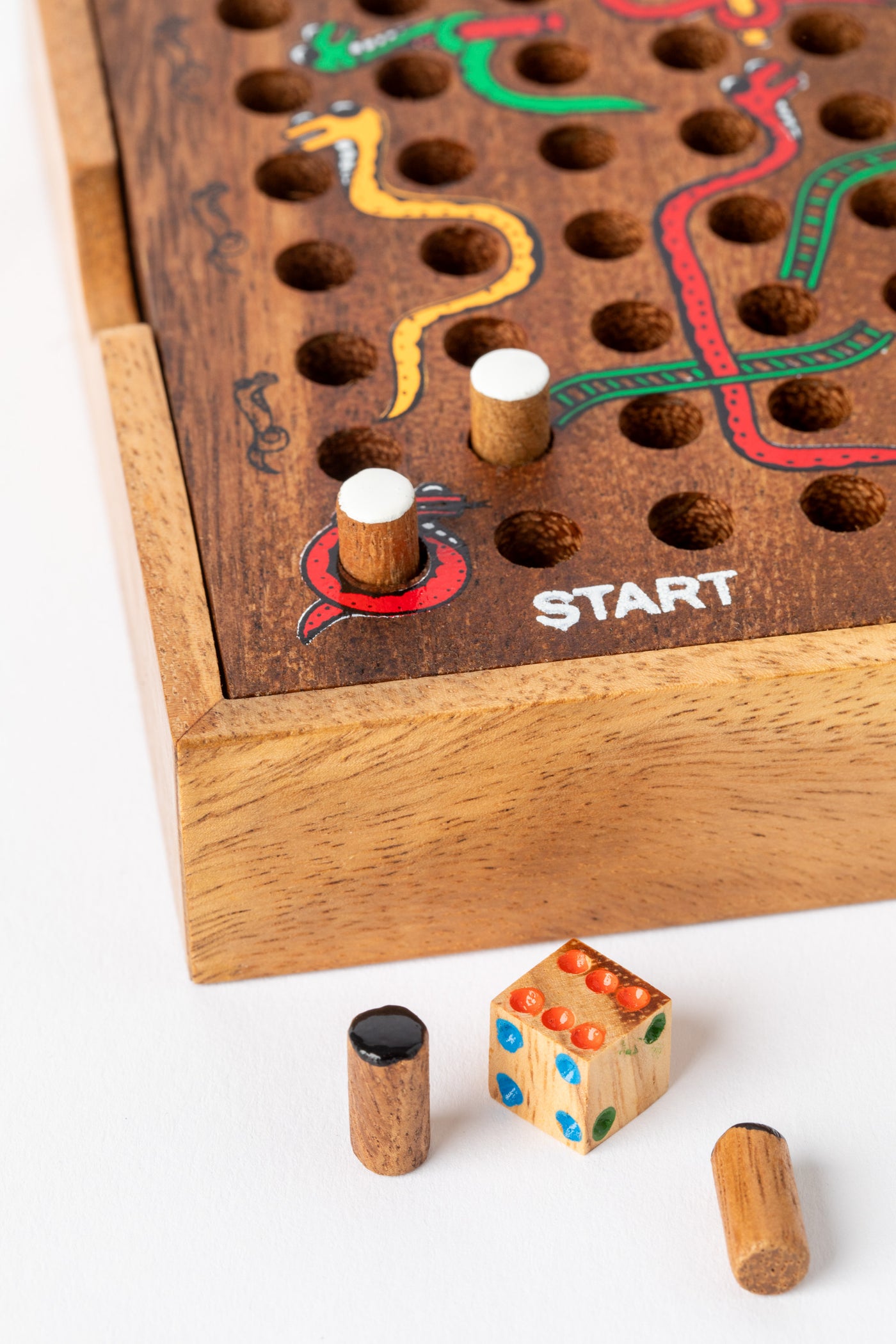 Close-up of wooden dice and player pegs beside a hand-painted snakes and ladders board — artisan wooden game gift for kids.