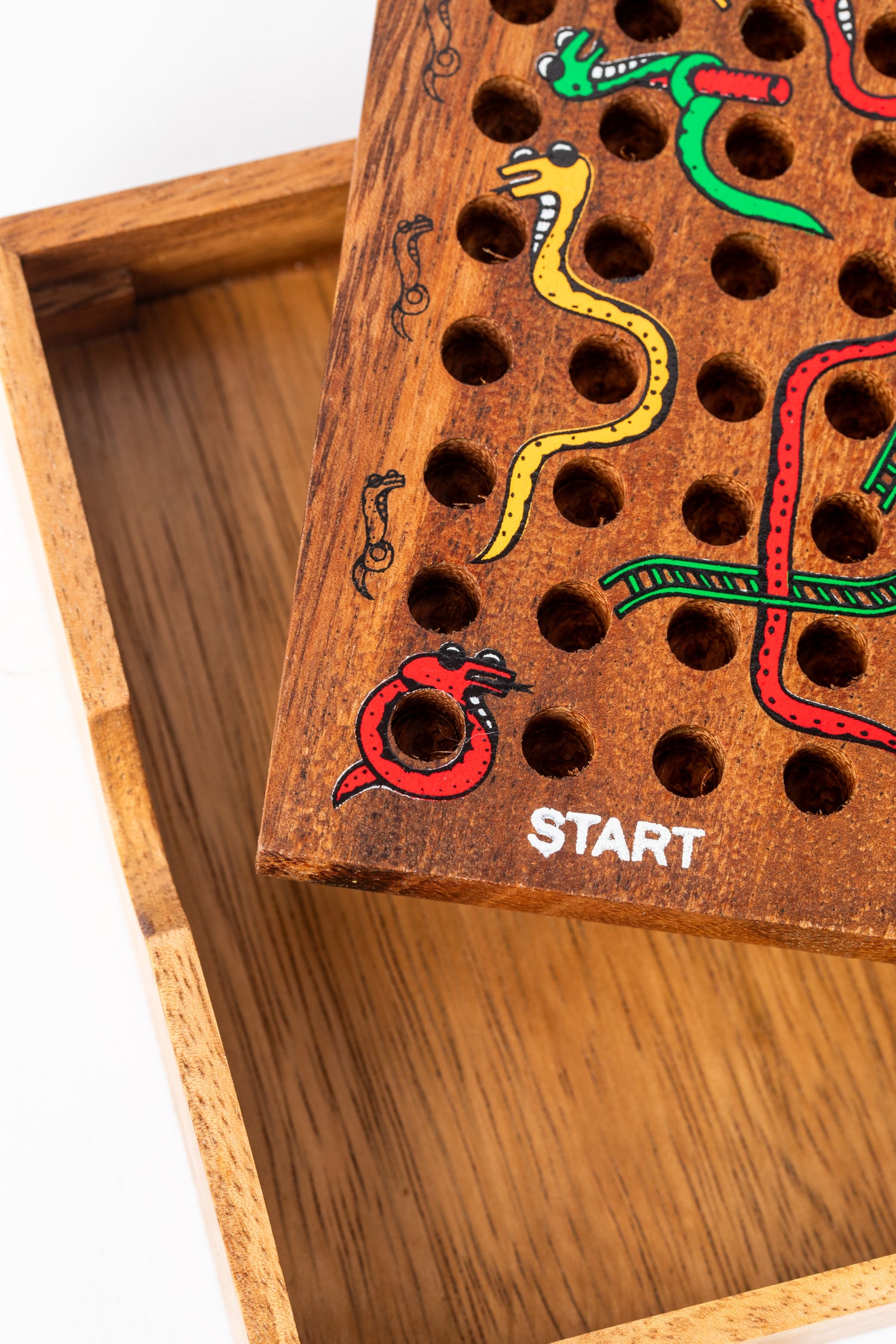 Close-up of hand-painted snakes and ladders details on carved wooden board — sustainable gift under $25.