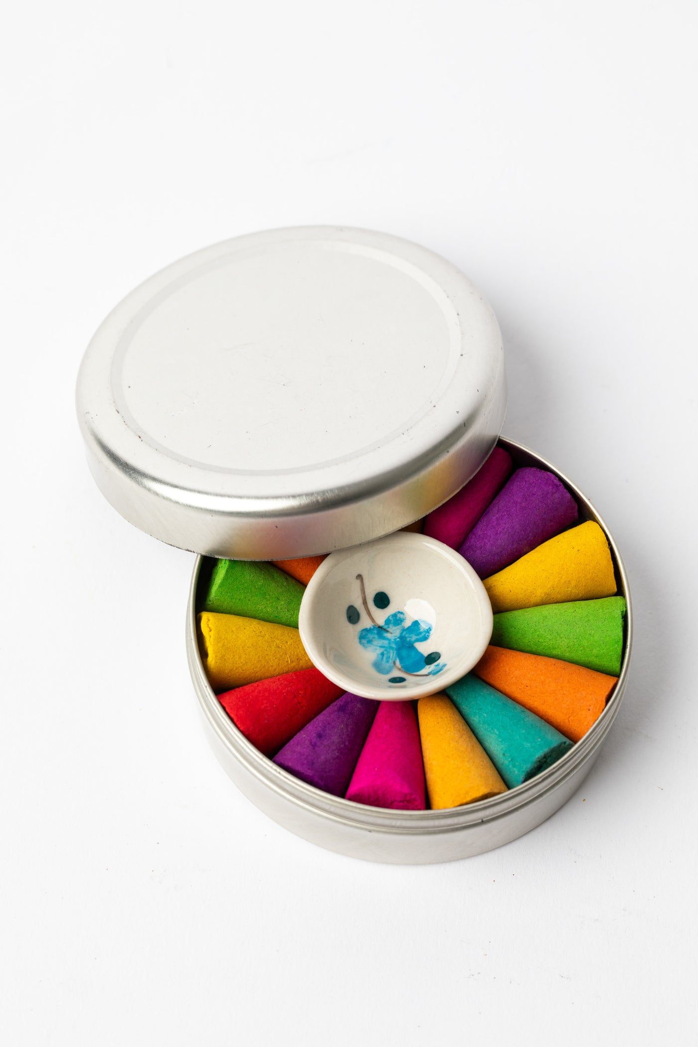 Top view of rainbow incense cones and ceramic holder inside reusable silver tin