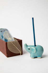 Close-up of blue ceramic elephant incense holder with incense stick burning beside box set