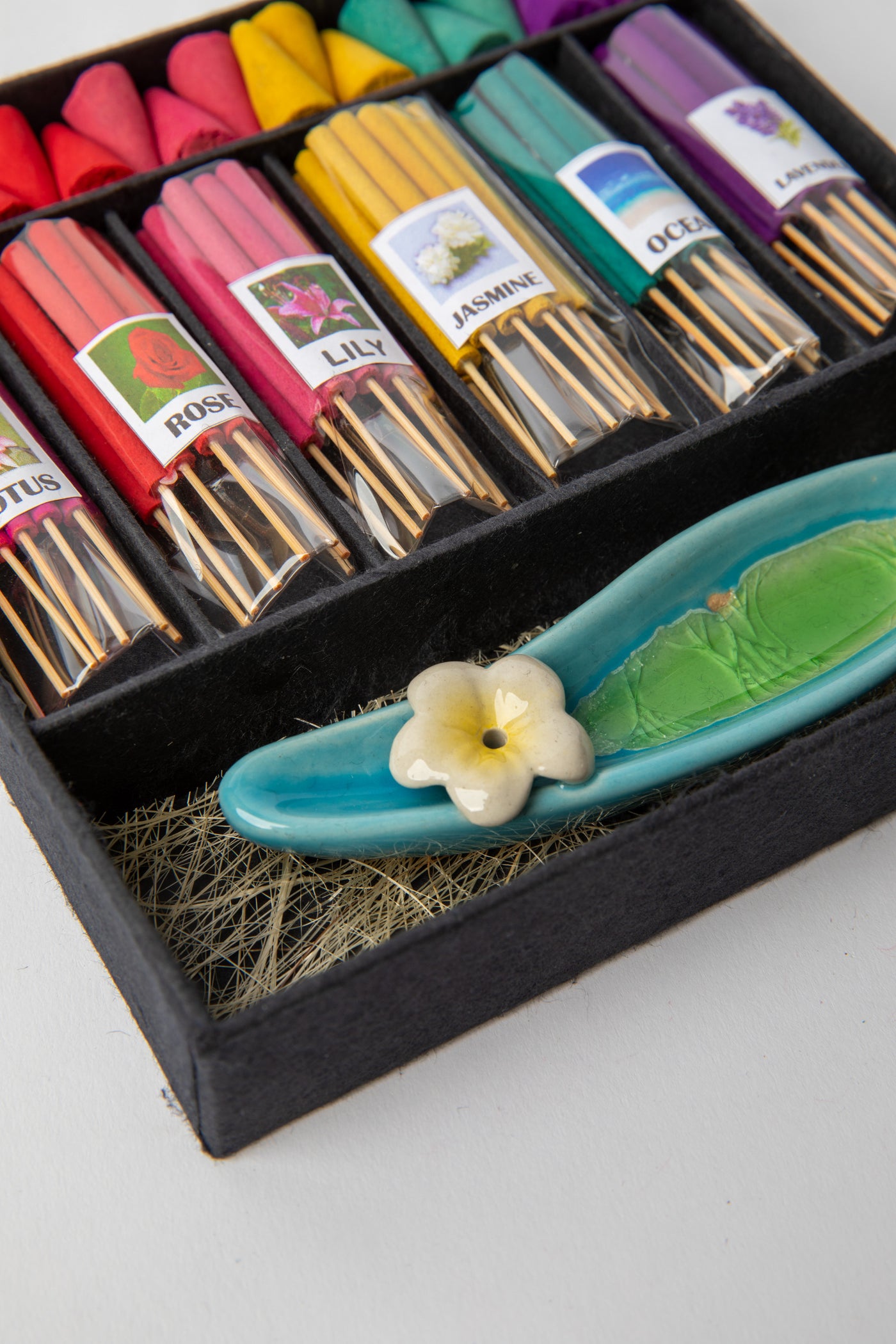 Colorful incense gift set with lotus, rose, lily, jasmine, ocean, and lavender scents arranged beside ceramic holder.