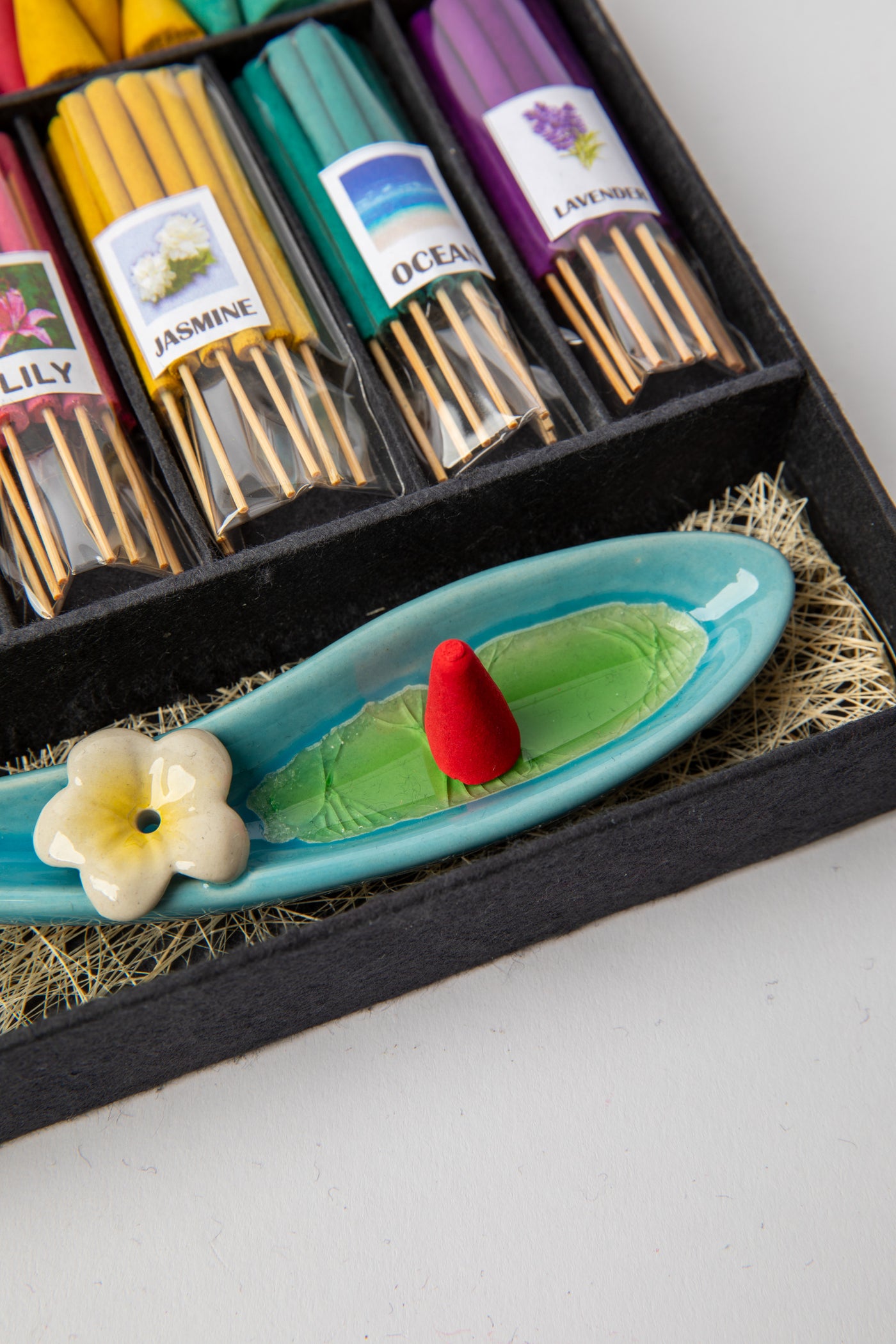 Leaf-shaped ceramic incense holder with flower detail and red incense cone ready for burning