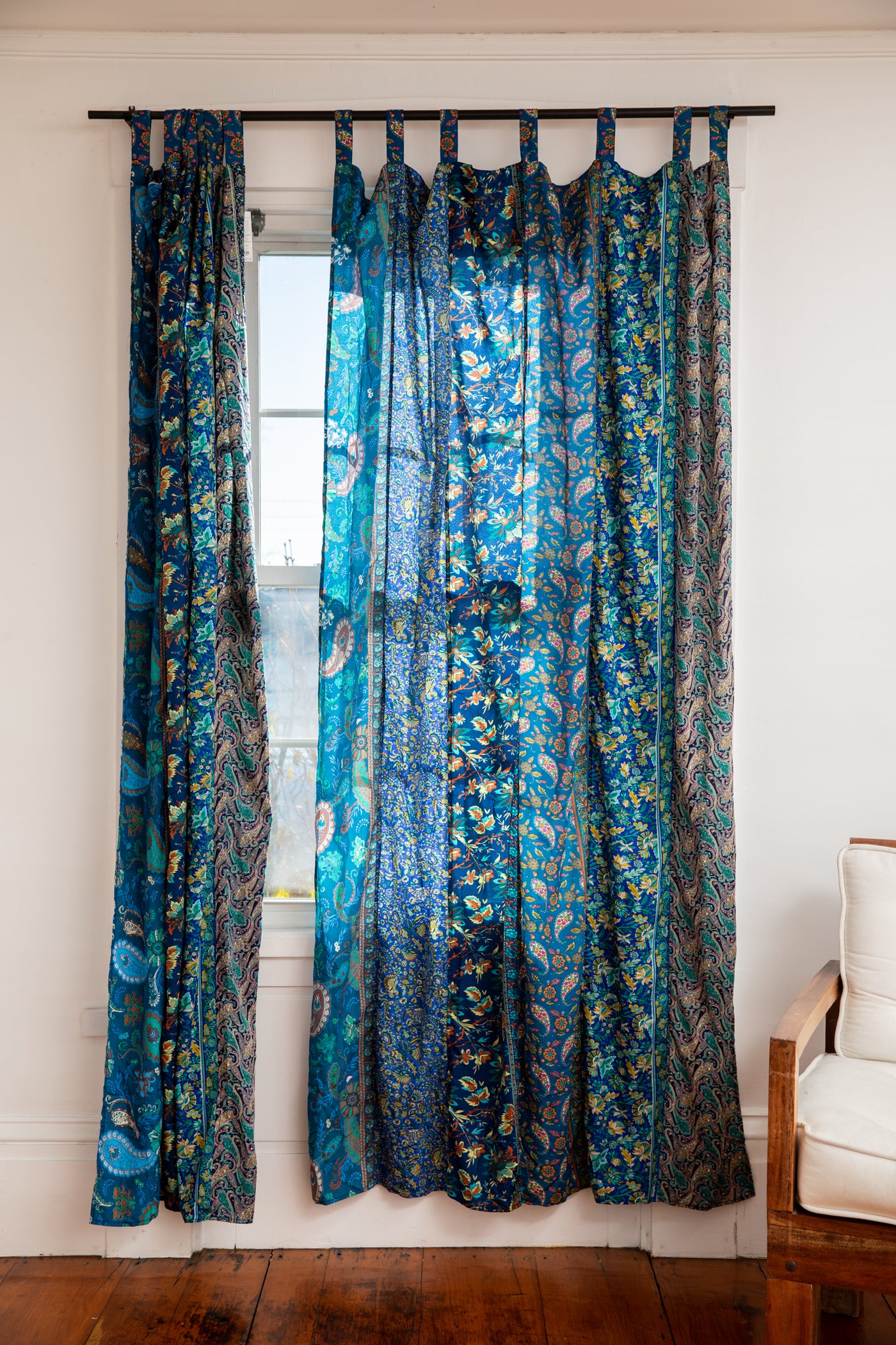 Vibrant sari silk curtains in blue hanging in front of a sunny window. 
