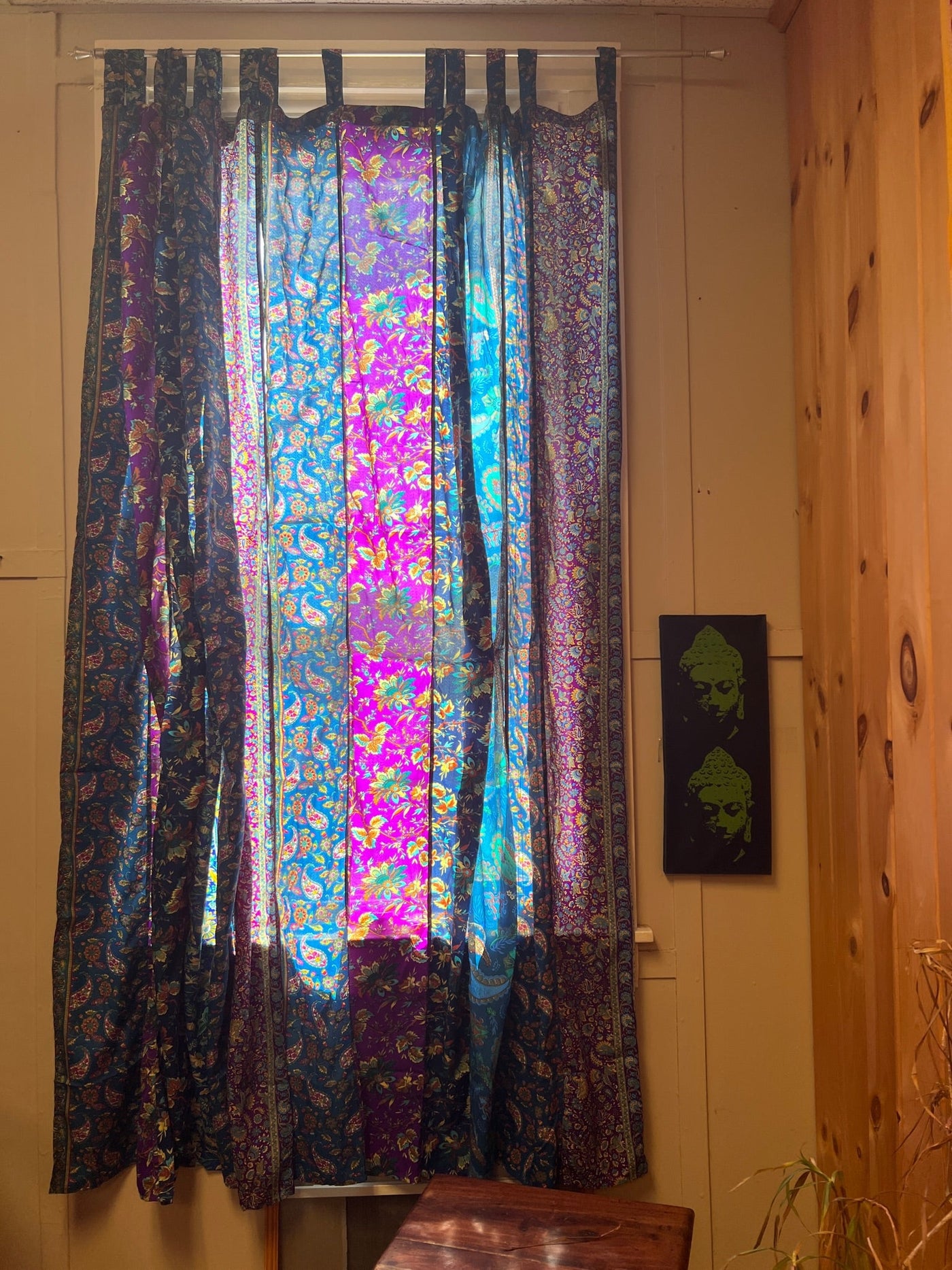 Blue and purple boho curtains hanging in front of a bright window. 