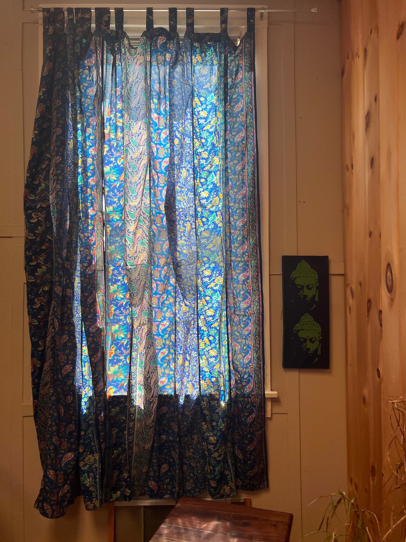Blue floral curtains made from sari silk hanging in front of a sunny window. 