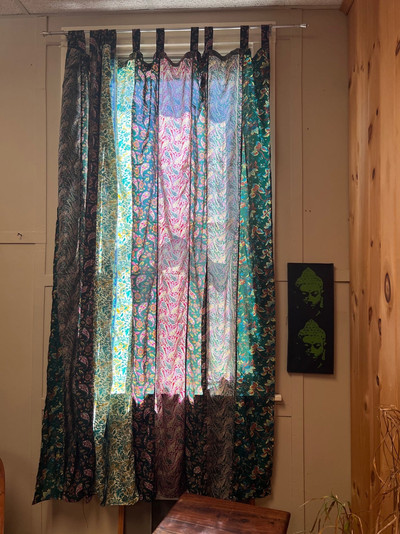 Green sari silk curtains with an intricate design hanging in front of a sunny window 