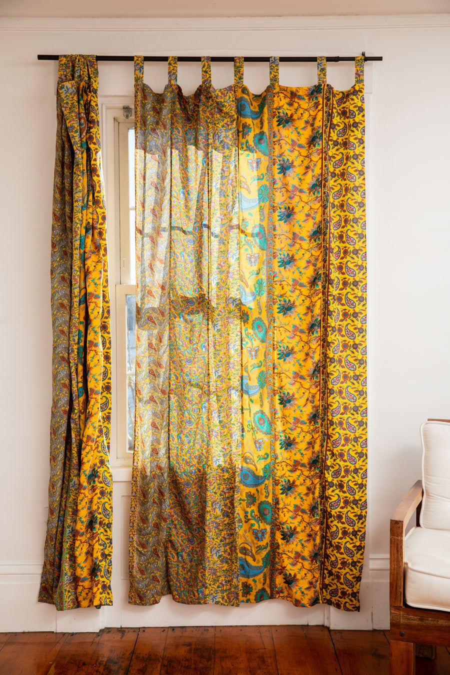 Beautiful sari silk curtains in yellow with a floral pattern hanging in front of a bright window. 