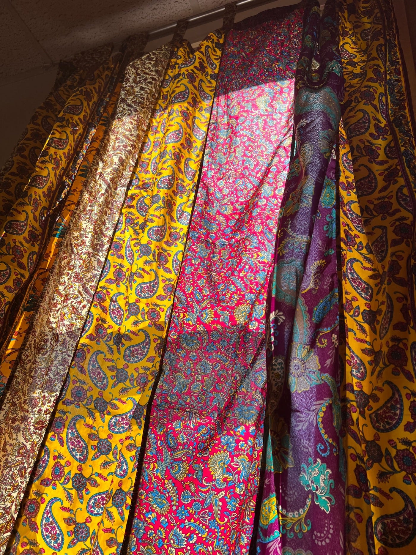 Floral boho curtains in red and yellow hanging in front of a sunny window. 