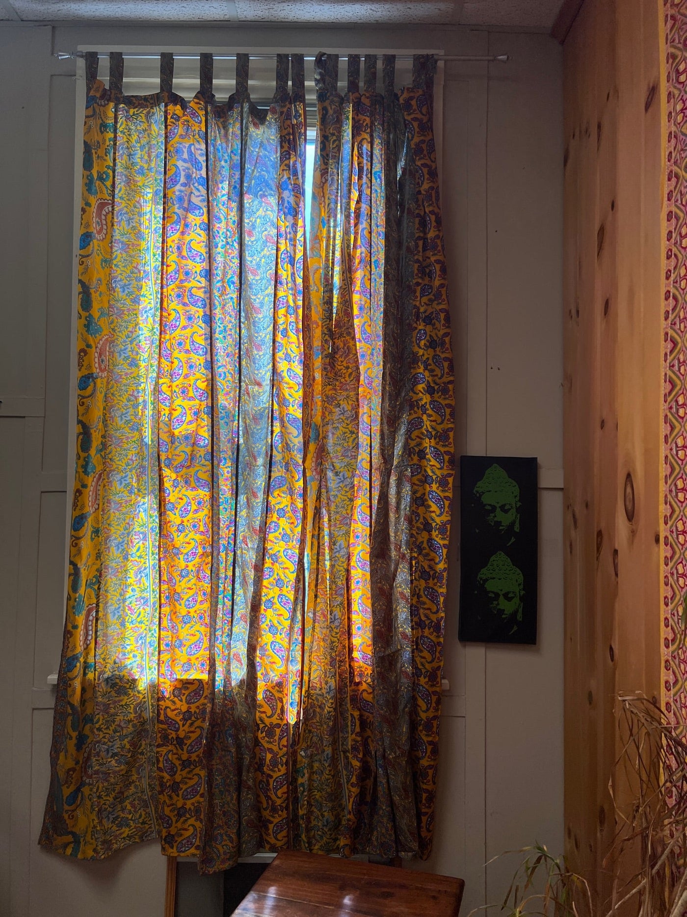Yellow bohemian curtains hanging in front of a sunny window. 